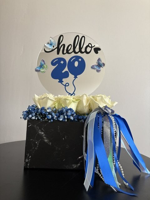 Caja negra con rosas blancas, flores azules, listones y globo “hello 20”