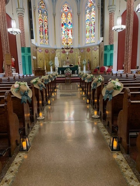 Pasillo de iglesia decorado con sombreros de paja, flores, listones verdes y faroles con velas